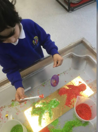 A young pupil from Nursery is pictured using paint to create a traffic light with different colours for 'stop' and 'go'.