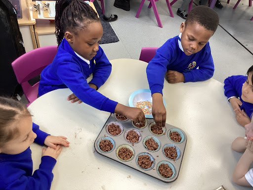 Five pupils from Reception are pictured sat together around a table, filling up a tray of cake cases with mixture.