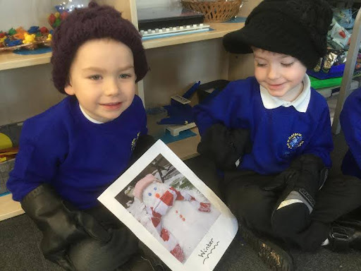 Two young boys from Nursery are pictured sitting on the floor wearing winter hats and gloves, whilst smiling for the camera.