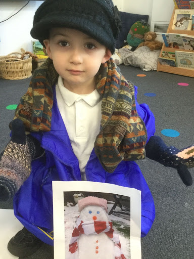A young boy from Nursery can be seen looking at the camera, whilst wearing a winter hat, scarf and gloves.