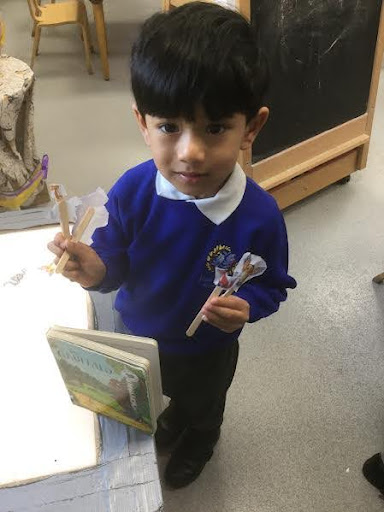A young boy is pictured smiling for the camera, whilst holding up some wooden lollipop sticks with pictures of characters from 'The Gruffalo' on them.