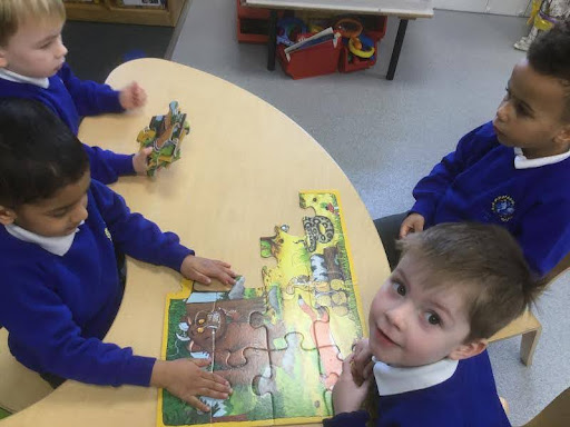 A group of four Nursery pupils are pictured sat around a table together, collaborating to complete a jigsaw puzzle of 'The Gruffalo'.
