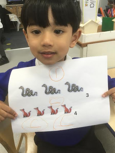 A young boy from Nursery is pictured smiling for the camera, as he shows some artwork he has created, inspired by characters from the children's storybook 'The Gruffalo'.