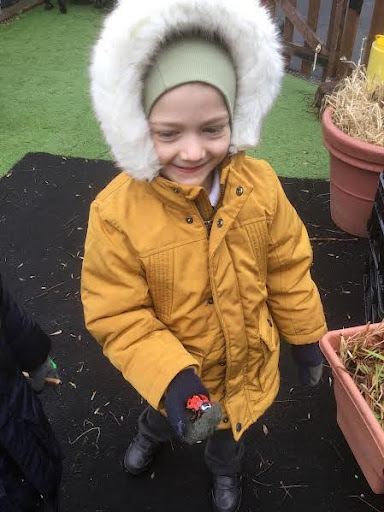 A young girl from Nursery is pictured outdoors, wearing her winter coat and smiling for the camera, whilst holding a toy Ladybird in her hand.