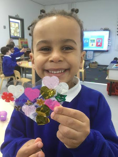 A young girl is pictured smiling for the camera, whilst showing a piece of artwork she has created for the camera.