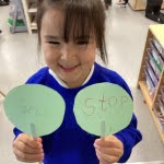 A young girl from Nursery is pictured smiling for the camera, whilst holding up two road safety signs she has created in class.