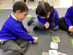 Three young pupils from Nursery are seen sat together on the floor playing with cards based on the topic of road safety.
