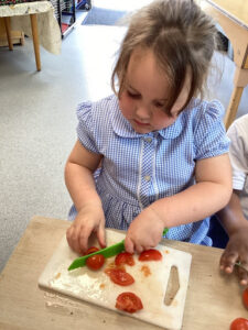 A young girl from Nursery is pictured chopping up some Tomatoes on a chopping board, using a plastic knife.