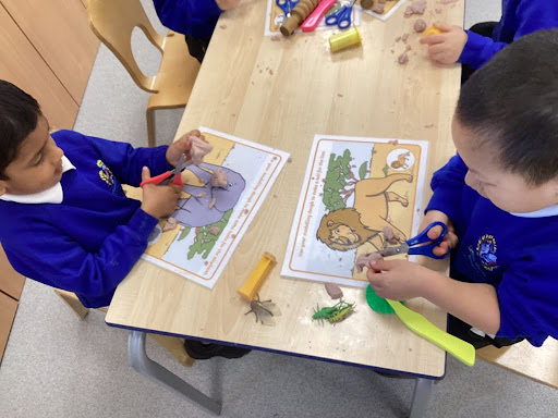 Two young boys from Nursery are pictured sitting opposite each other at a desk, sticking stickers onto pictures of safari animals.