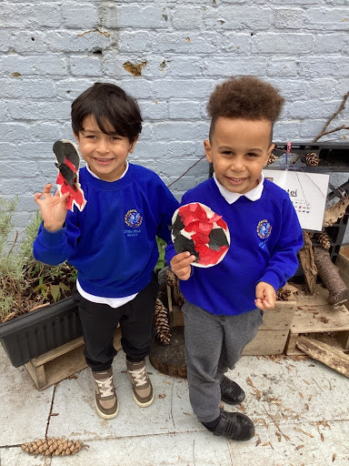 Two young boys from Nursery are pictured smiling together outdoors, whilst holding up pictures of Ladybirds they have created.