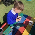 A young boy from Nursery is pictured filling a paper cup with soil ready to plant Sunflower seeds in it.